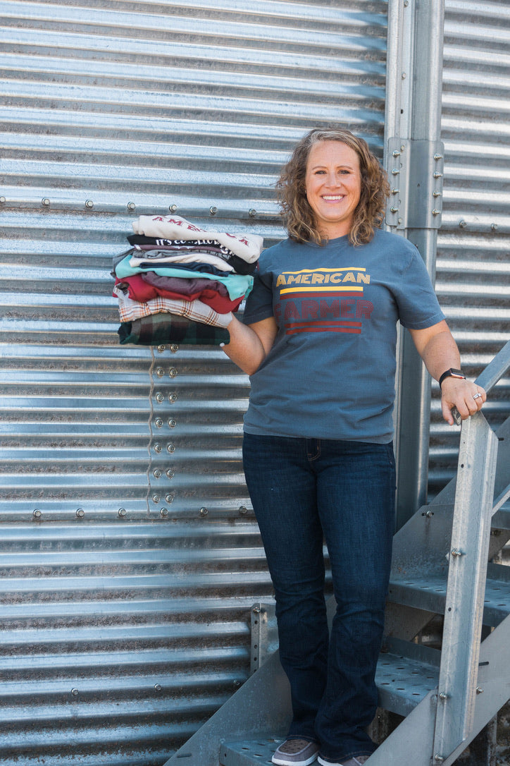 Person holding a stack of clothes in front of a corrugated metal wall