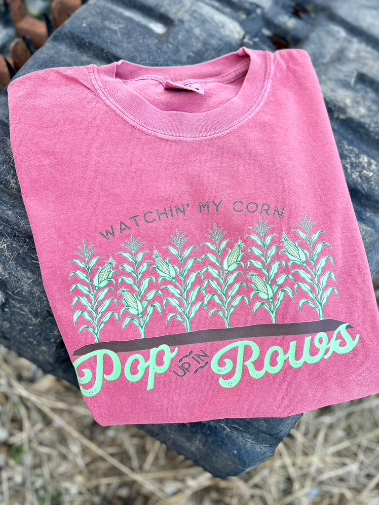 Pink t-shirt with corn plant design and text on a textured surface