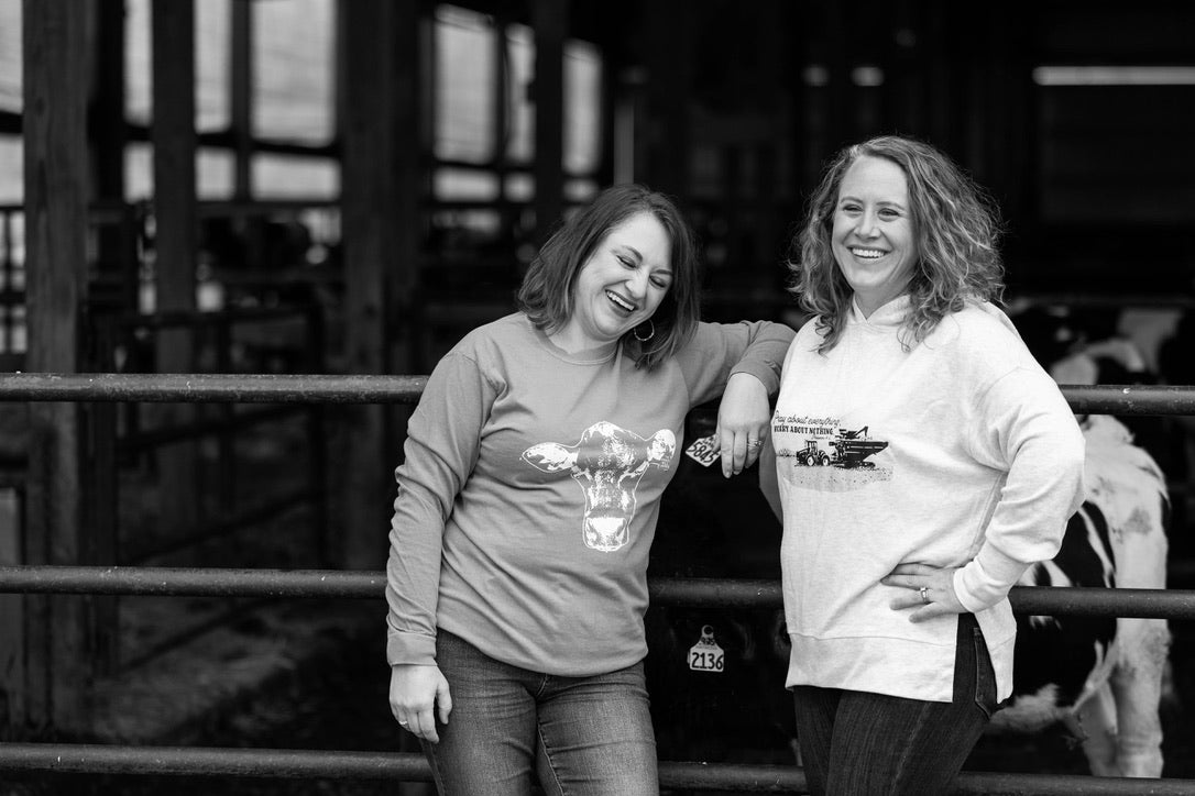 Two women standing next to each other in a barn-like setting, holding glasses.