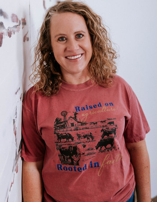 Woman wearing a red t-shirt with graphic design and text, standing against a white wall.