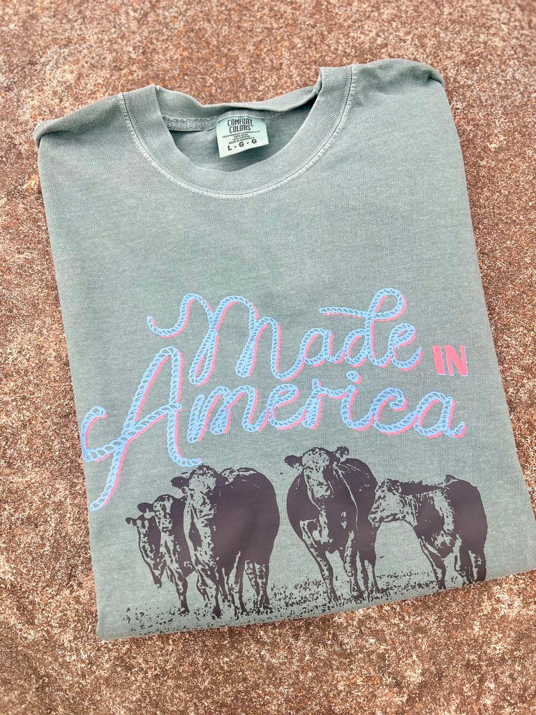 Folded t-shirt with 'Made in America' text and cow graphics on a textured surface