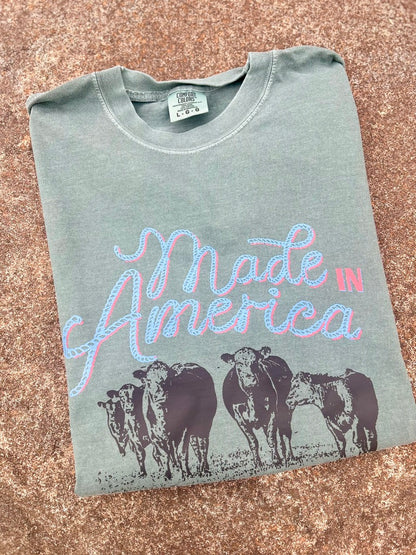 Folded t-shirt with 'Made in America' text and cow graphics on a textured surface