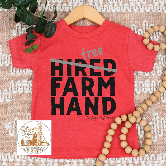 Red t-shirt with 'free hired farm hand' text on a textured surface with decorative elements.