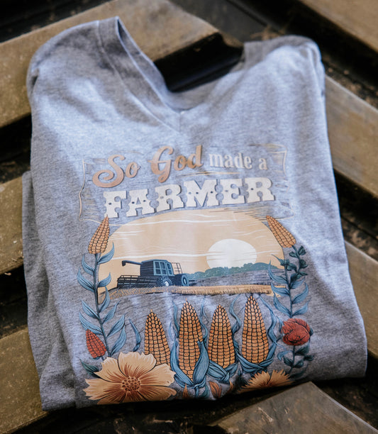 Folded gray t-shirt with 'So God Made a Farmer' design on a wooden surface