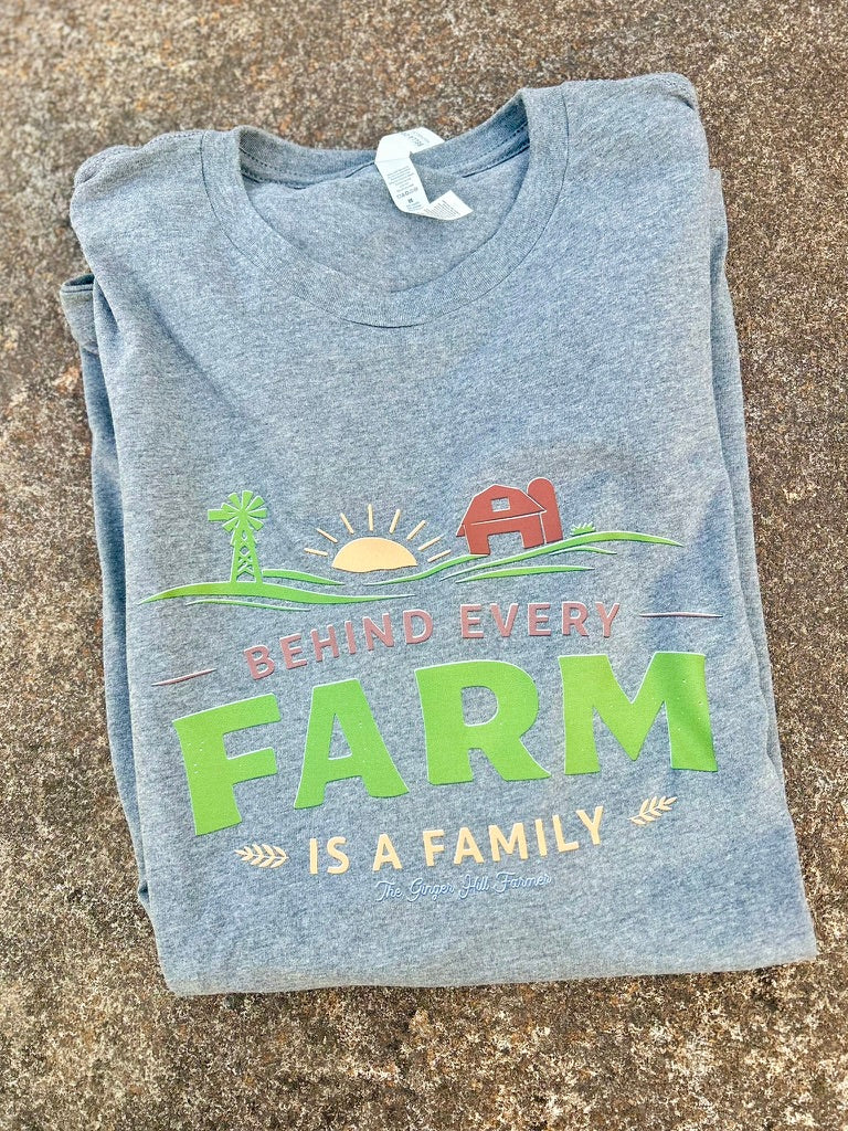 Folded grey t-shirt with a farm-themed graphic and text on a concrete surface
