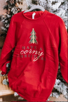 Red sweatshirt with Christmas tree design and text, hanging against a snowy tree background