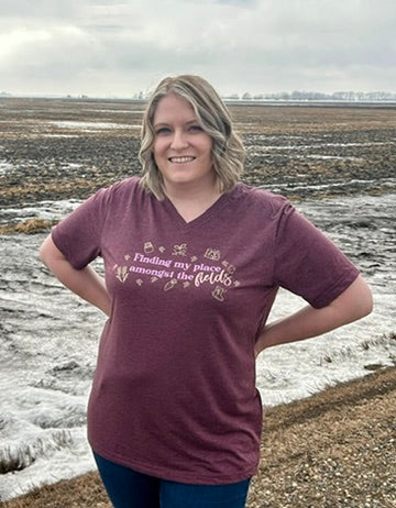 Woman wearing a purple t-shirt with text standing in a field.