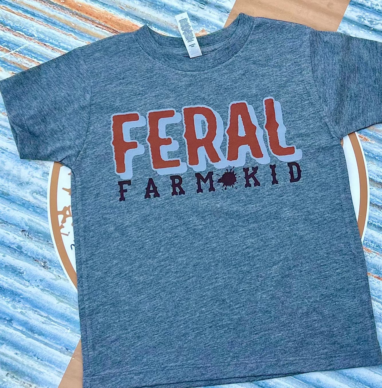 grey t-shirt with 'FERAL FARM KID' text on a striped background