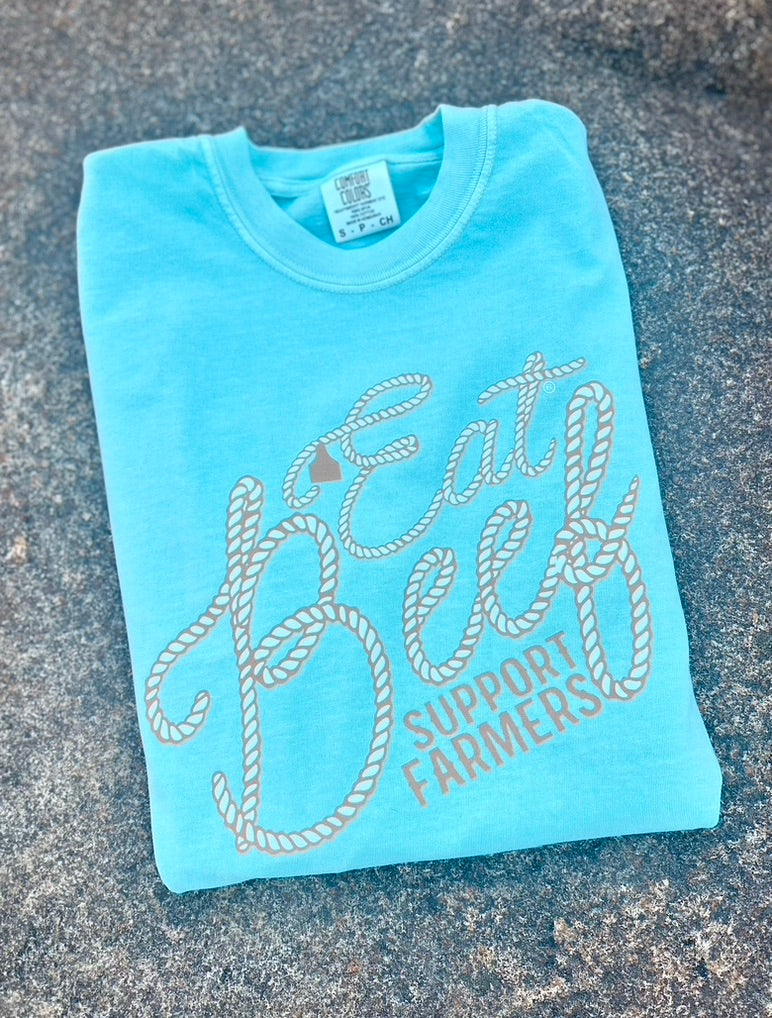 Light blue t-shirt with 'Eat Beef Support Farmers' text on a textured surface