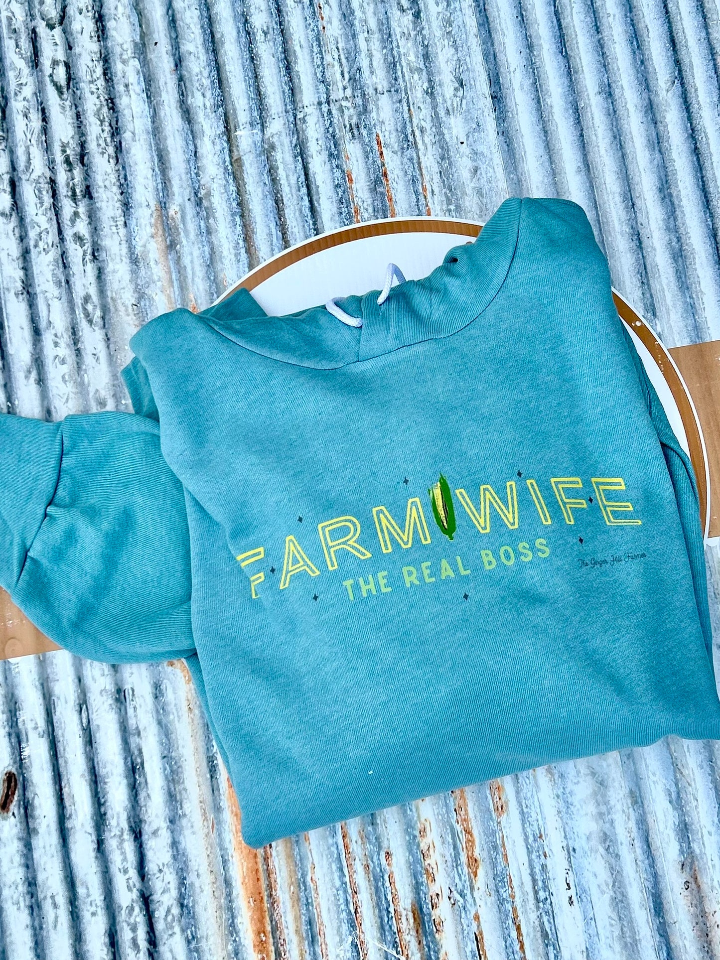 Teal sweatshirt with 'Farmwife, The Real Boss' text on a rustic wooden background