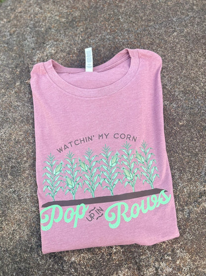 Folded purple t-shirt with green text and graphics on a gray surface