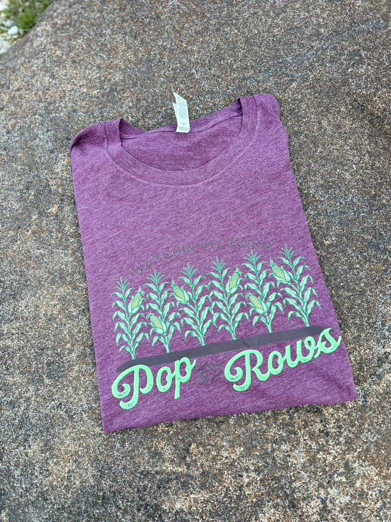 Purple t-shirt with green text and design on a stone surface