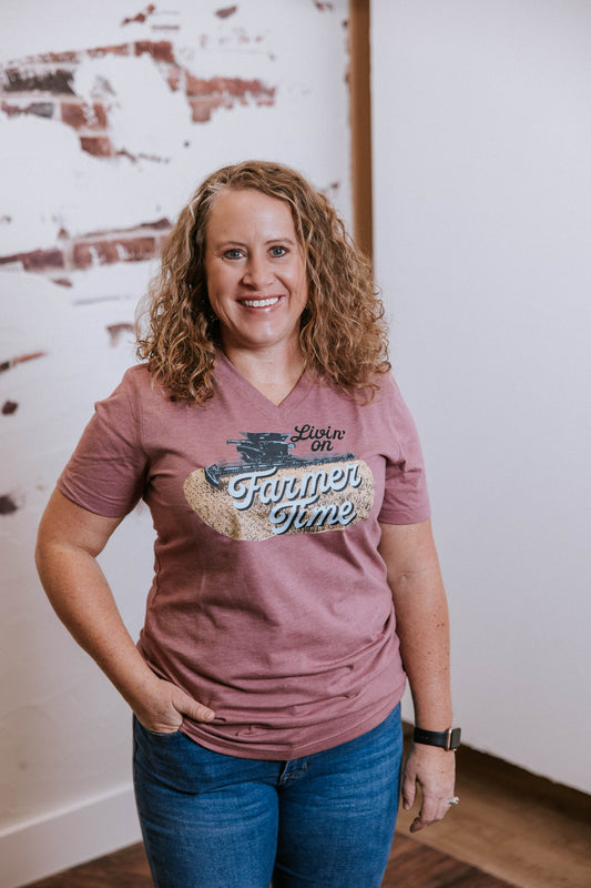 Woman wearing a 'Livin' on Farmer Time' t-shirt in a room with a rustic wall.
