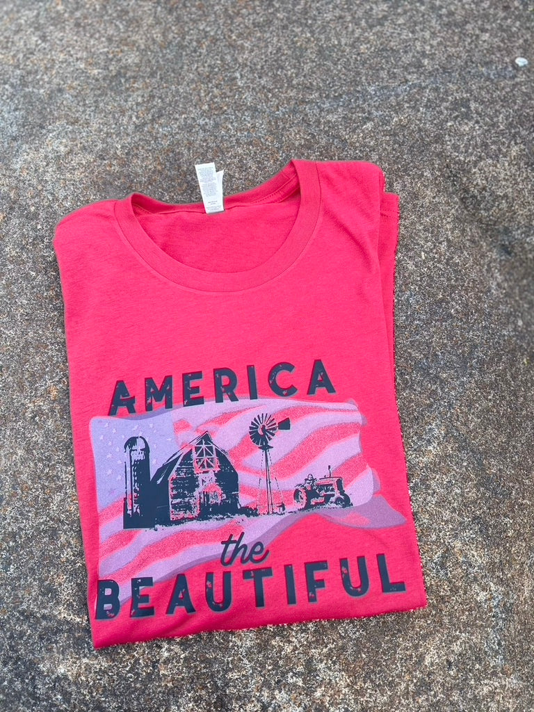 Folded red t-shirt with 'America the Beautiful' graphic on a textured surface