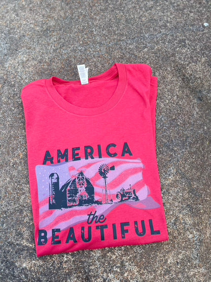 Folded red t-shirt with 'America the Beautiful' graphic on a textured surface