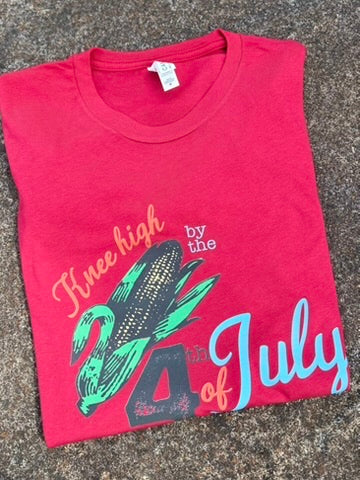 Folded red t-shirt with corn graphic and text on a textured surface