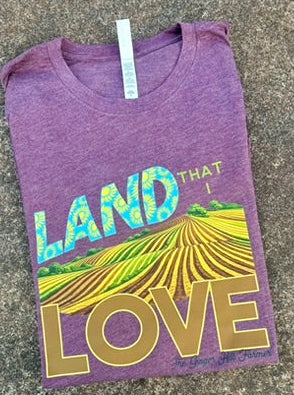 Maroon t-shirt with 'Land That I Love' design on a textured surface