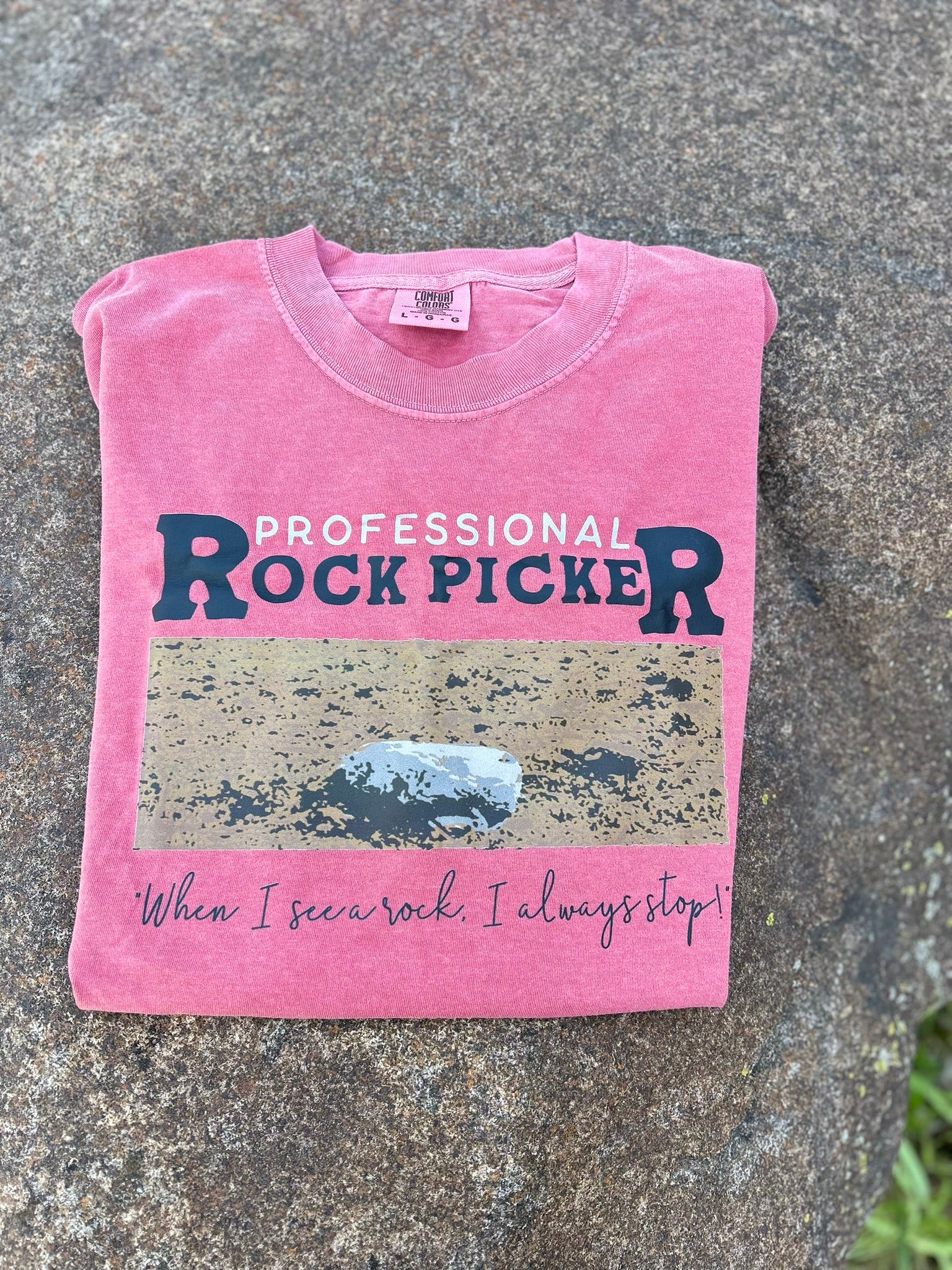 Pink t-shirt with 'Professional Rock Picker' text on a stone surface