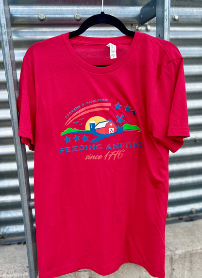 Red t-shirt with 'Feeding America' logo on a hanger against a metal wall.