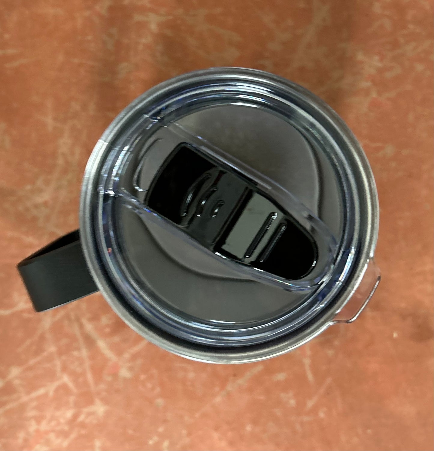 Close-up of a metal mug with a black handle on a brown surface