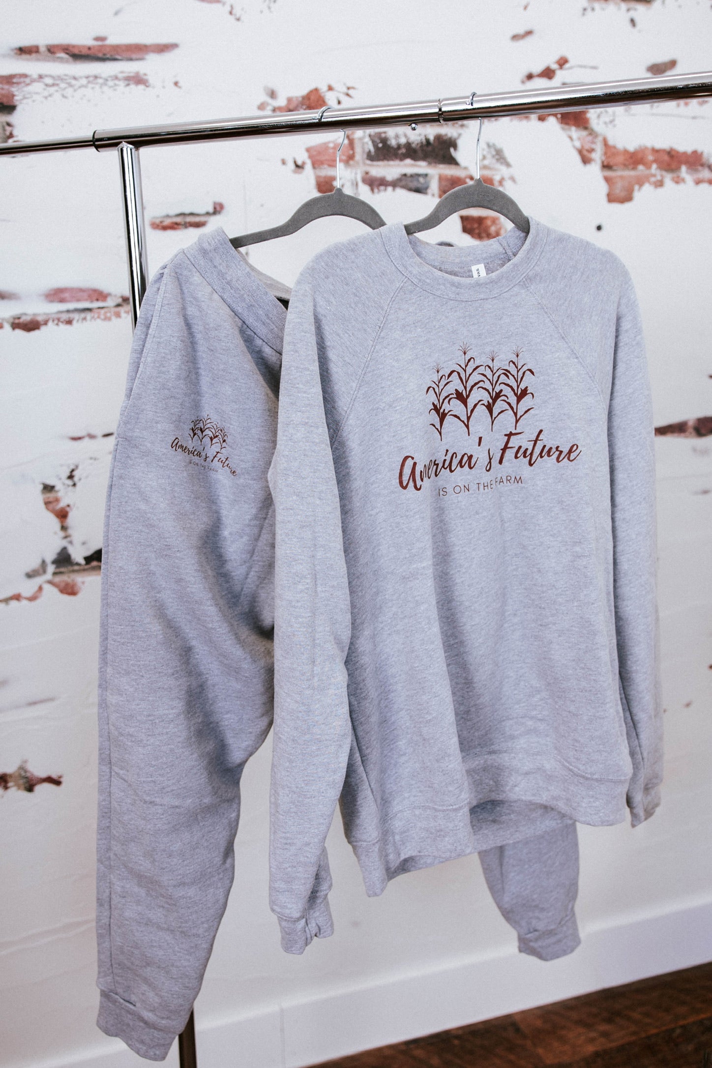 Gray sweatshirt with text on a hanger against a rustic wall.