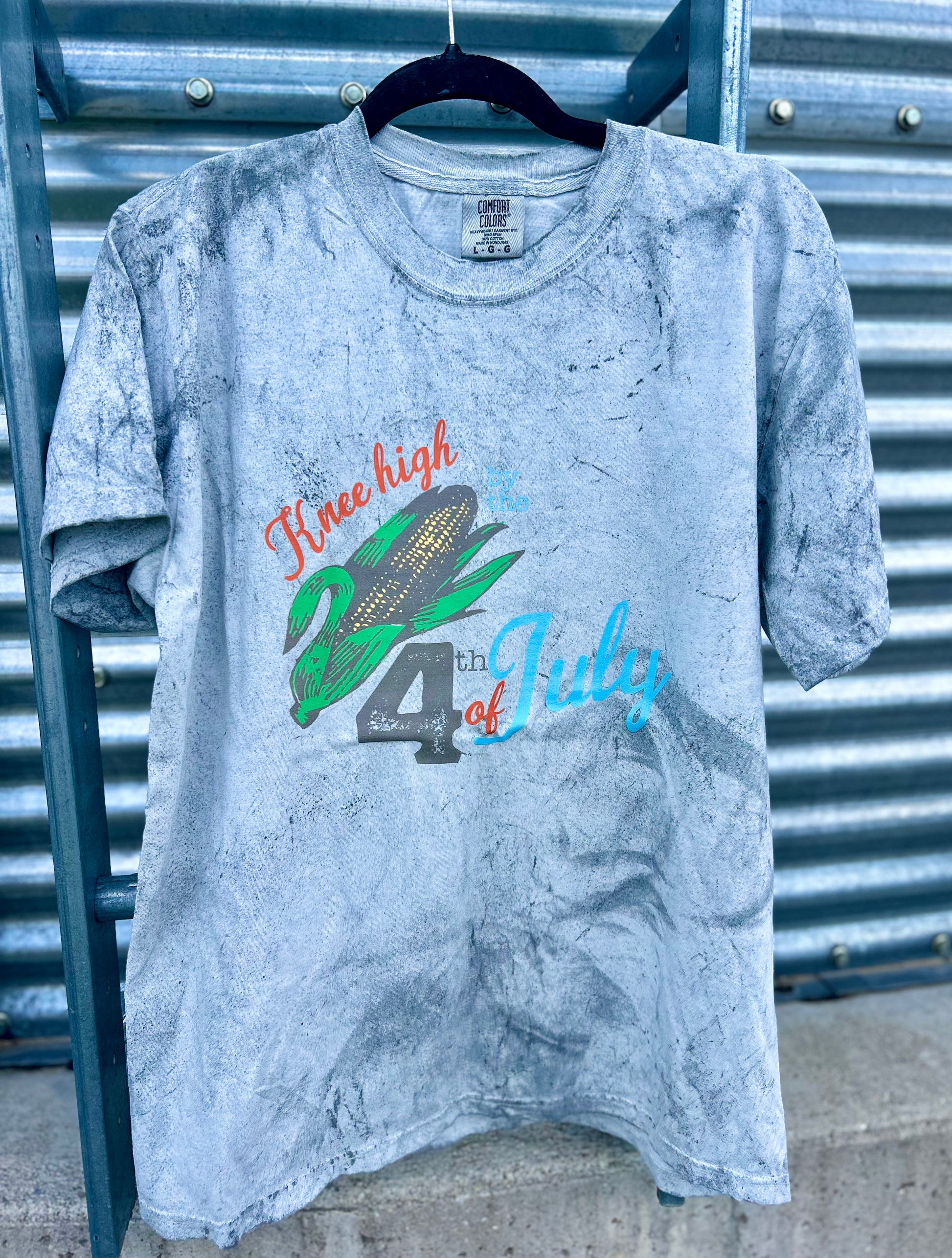 Gray t-shirt with corn graphic and text on a metal surface