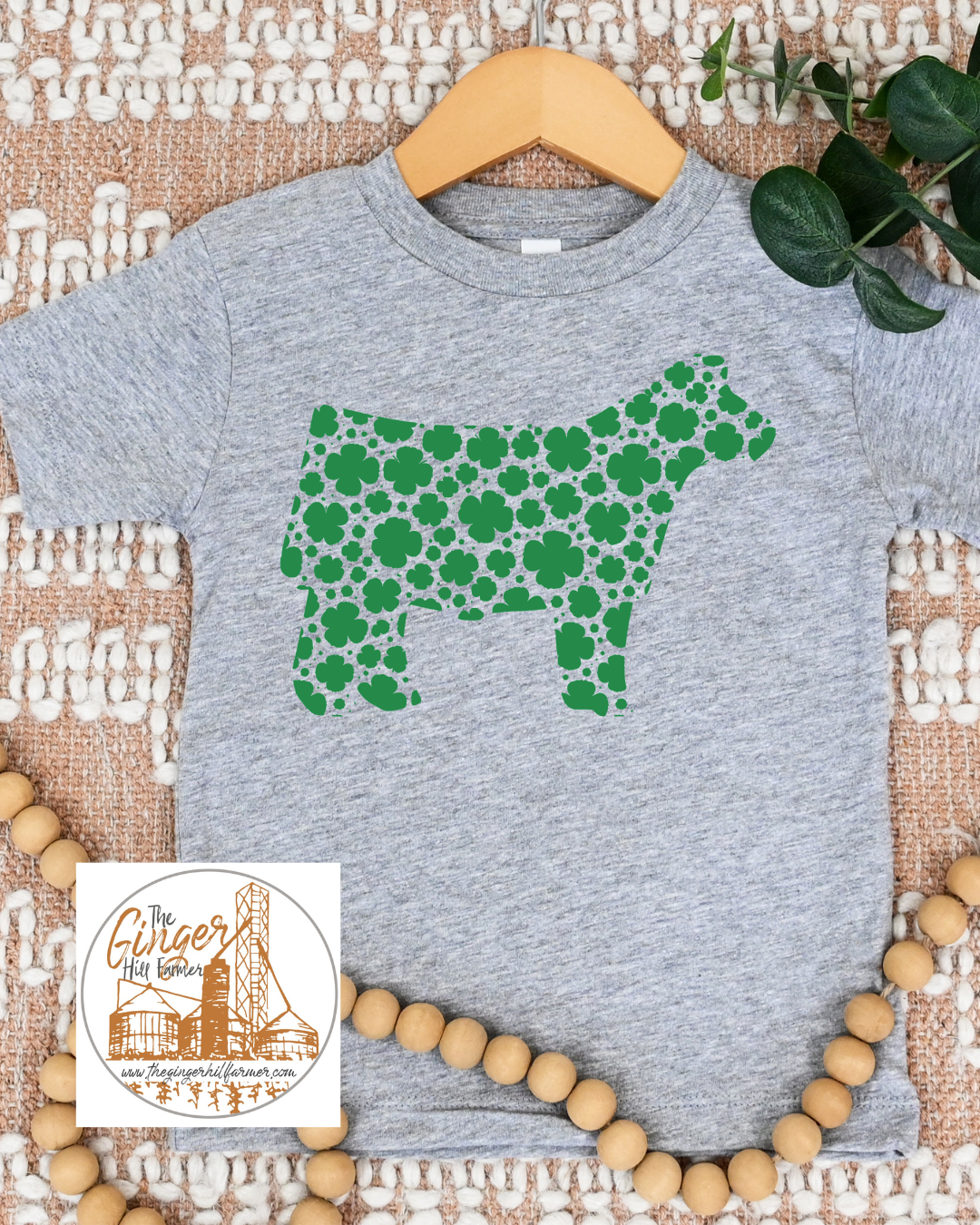 Gray t-shirt with green cow silhouette made of shamrock pattern on a textured surface.