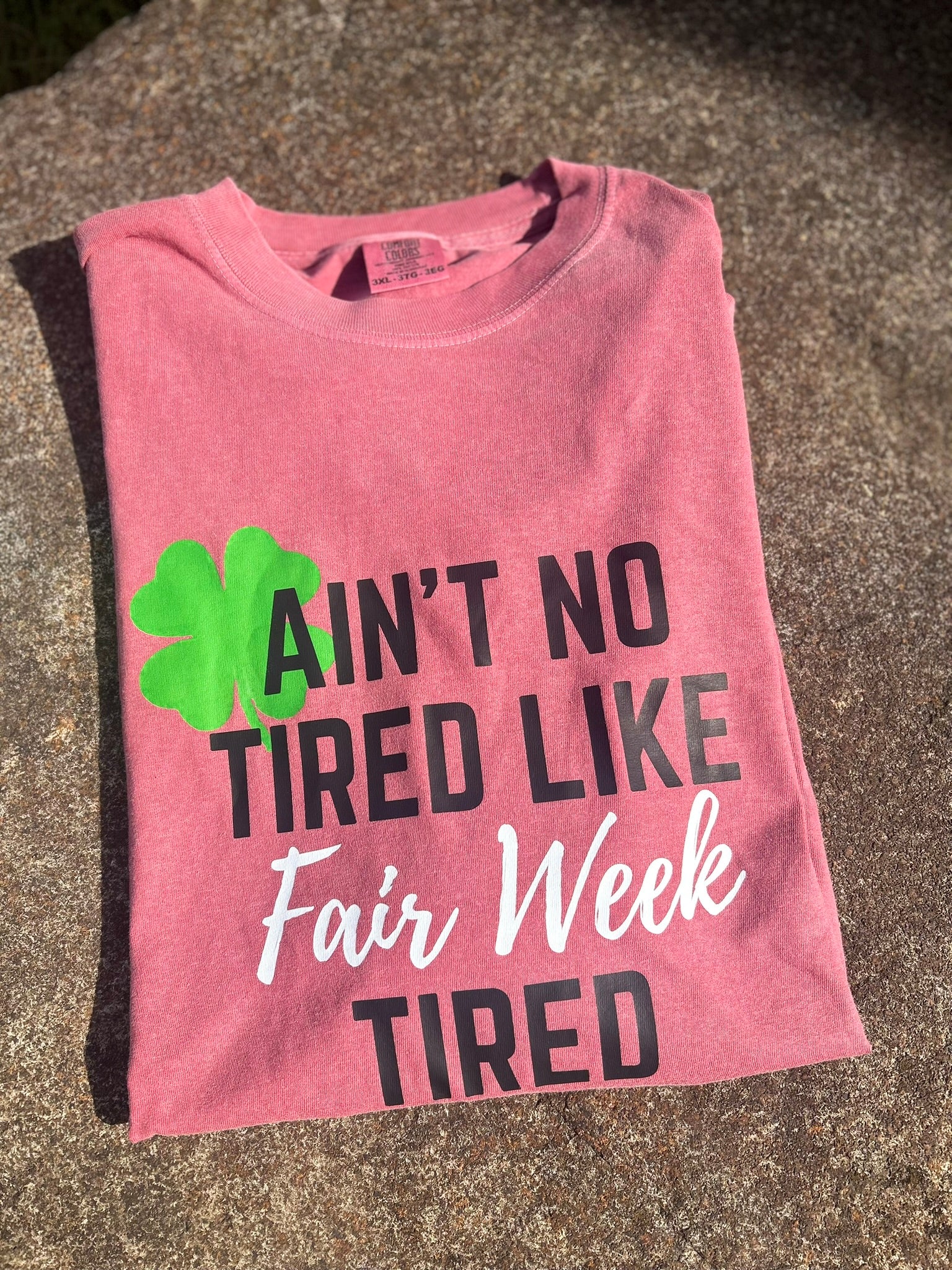 Pink t-shirt with text and clover graphic on a concrete surface