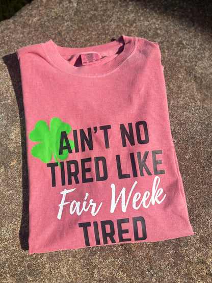 Pink t-shirt with text and clover graphic on a concrete surface