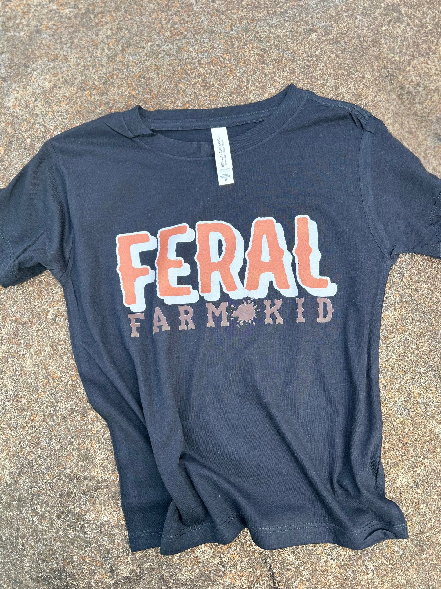 black t-shirt with 'FERAL FARM KID' text on a concrete surface