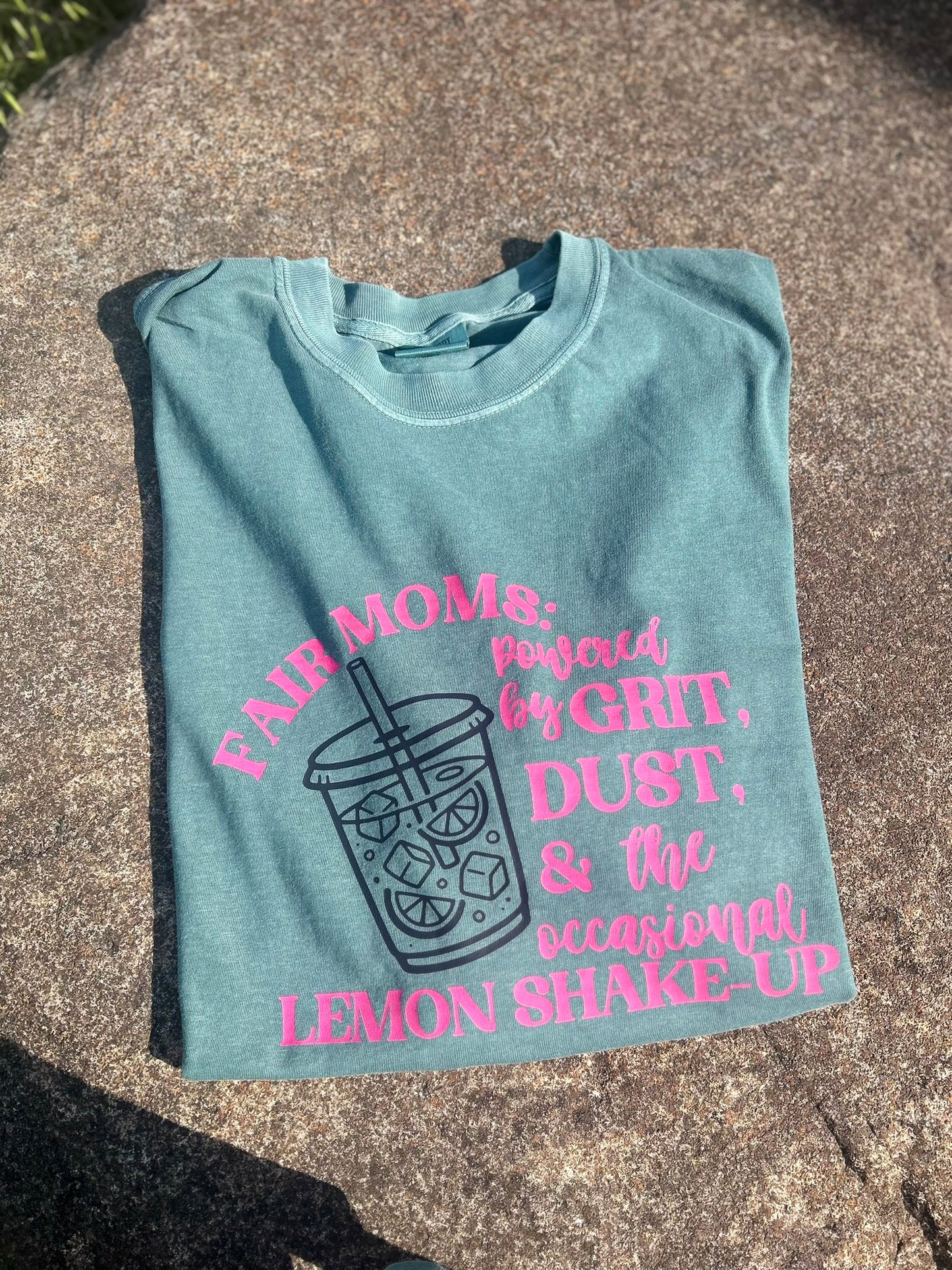 Light blue t-shirt with pink text and graphic on a concrete surface