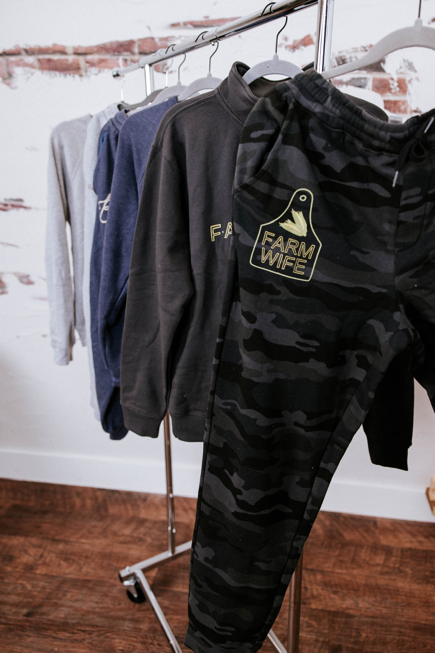 Black hoodie and camouflage pants with 'Farm Wife' graphic on a clothing rack.