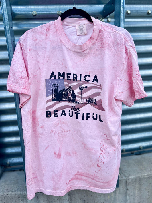 Pink t-shirt with 'America the Beautiful' graphic on a metal background