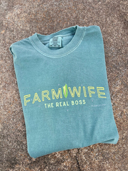 Folded teal t-shirt with 'Farmwife, The Real Boss' text on a textured surface