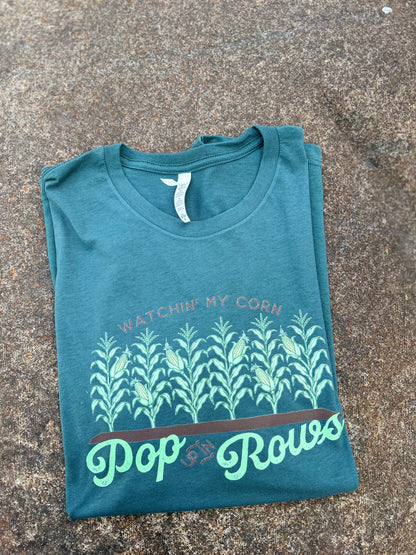 Folded teal t-shirt with corn plant design and text on a concrete surface