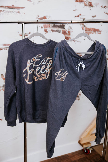 Navy sweatshirt and hoodie with text on hangers against a rustic wall.