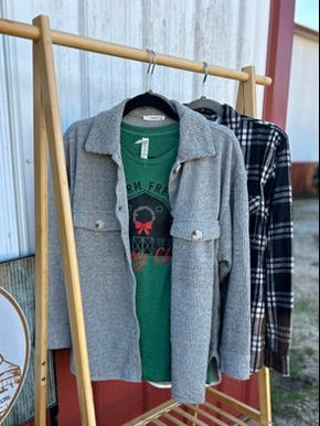 Clothing rack with coats and a green shirt in front of a building with a sign.