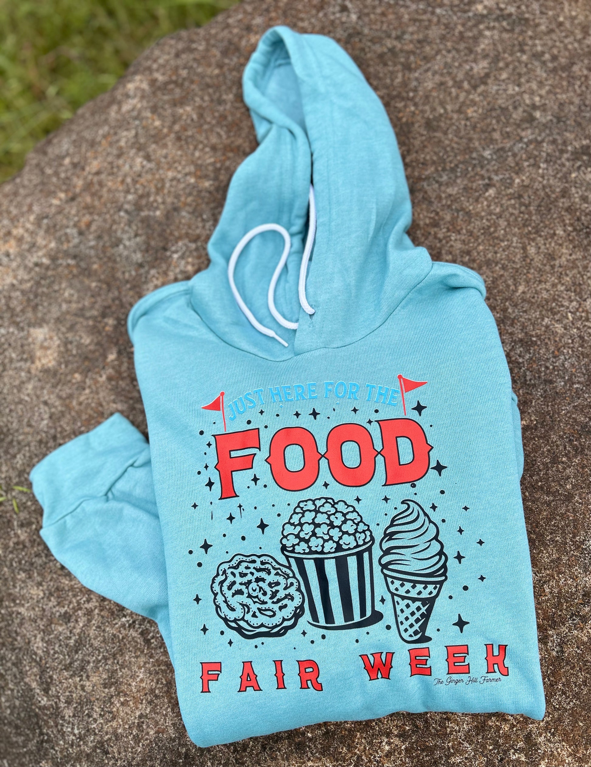 Light blue hoodie with 'Food Fair Week' text and graphics on a stone surface