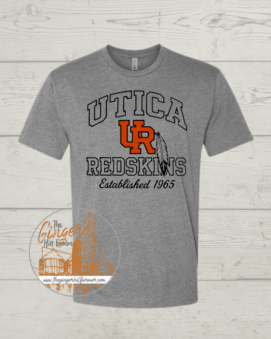 Gray t-shirt with 'UTICA REDSKINS Established 1965' text and logo on a wooden surface.