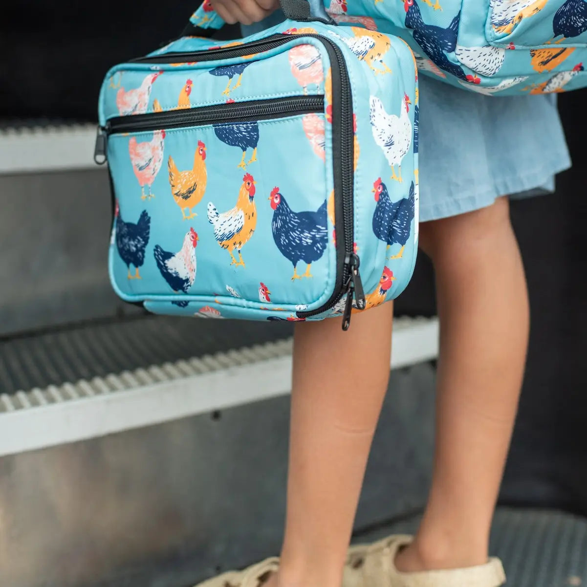 Person holding a blue lunch bag with chicken pattern, wearing a denim skirt.
