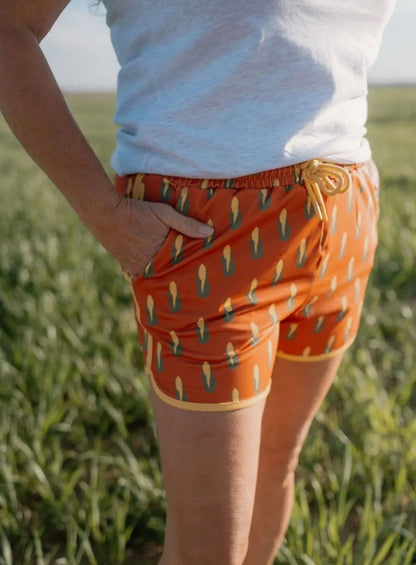 Person wearing orange shorts with a pattern, standing in a grassy field.