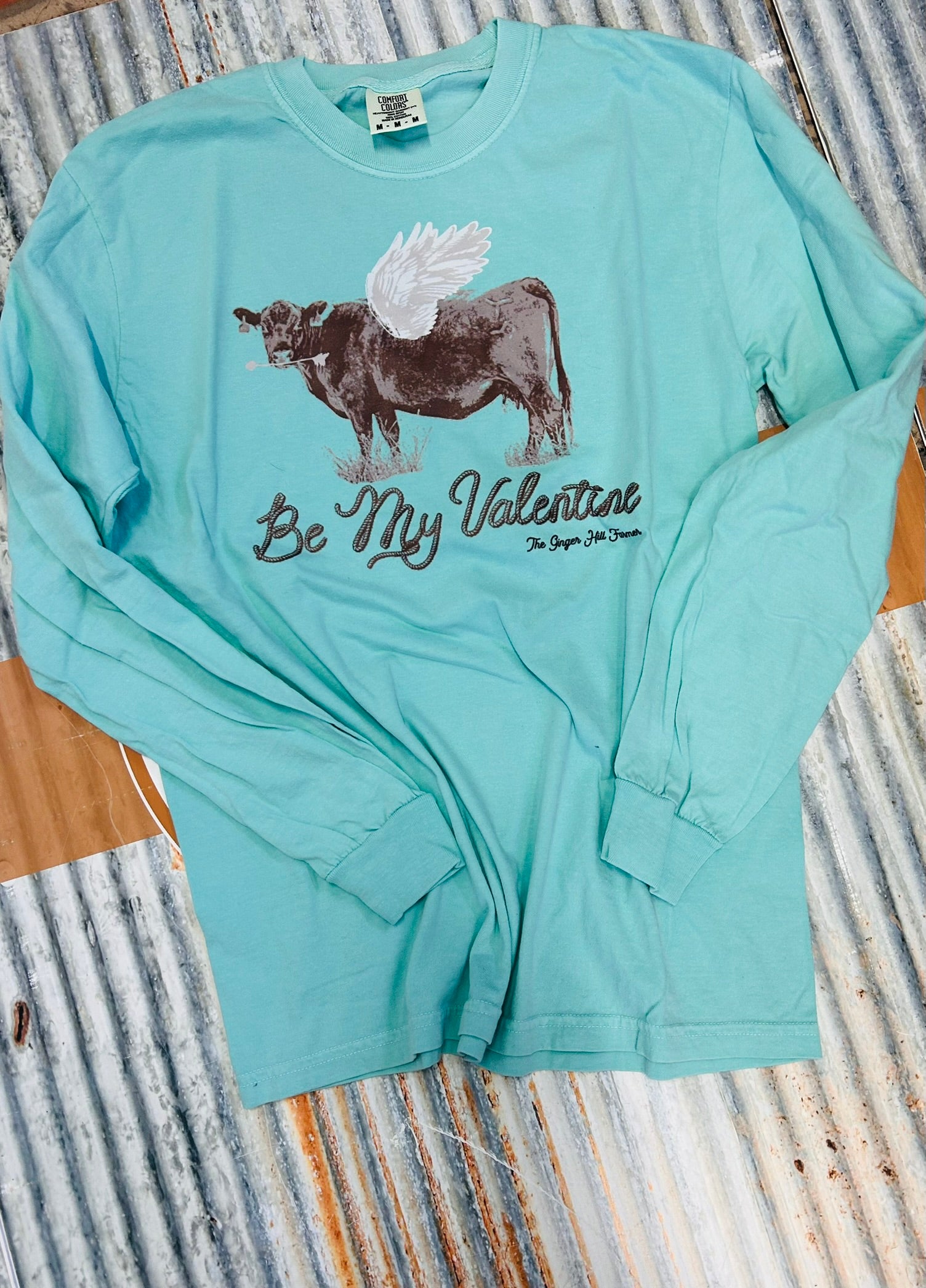 Light blue long-sleeve shirt with a cow graphic and text on a striped background