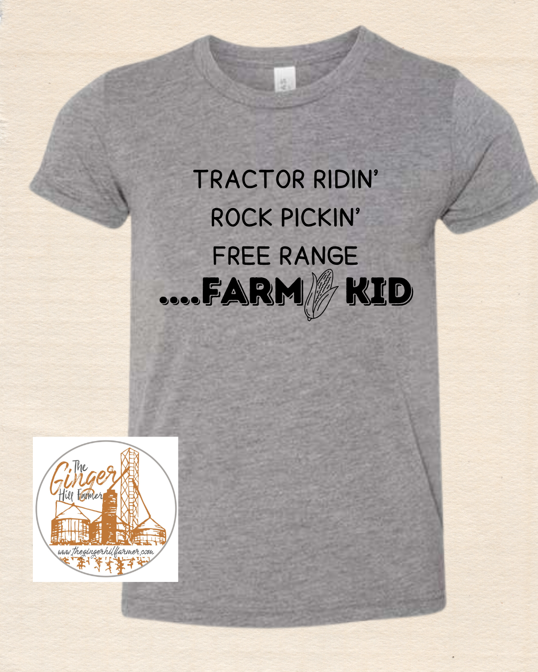 Gray t-shirt with black text 'Tractor Ridin' Rock Pickin' Free Range Farm Kid' on a beige background