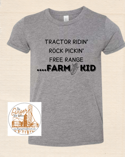 Gray t-shirt with black text 'Tractor Ridin' Rock Pickin' Free Range Farm Kid' on a beige background