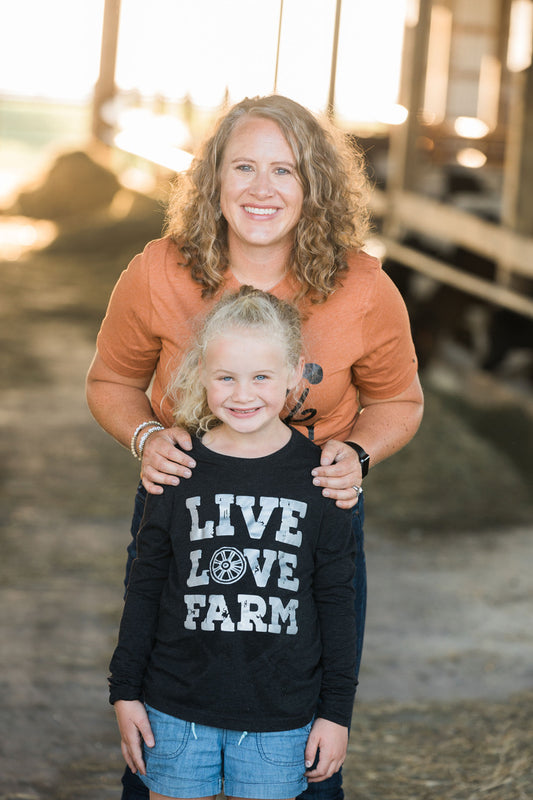 Woman and child standing together with a 'Live Love Farm' shirt, blurred background