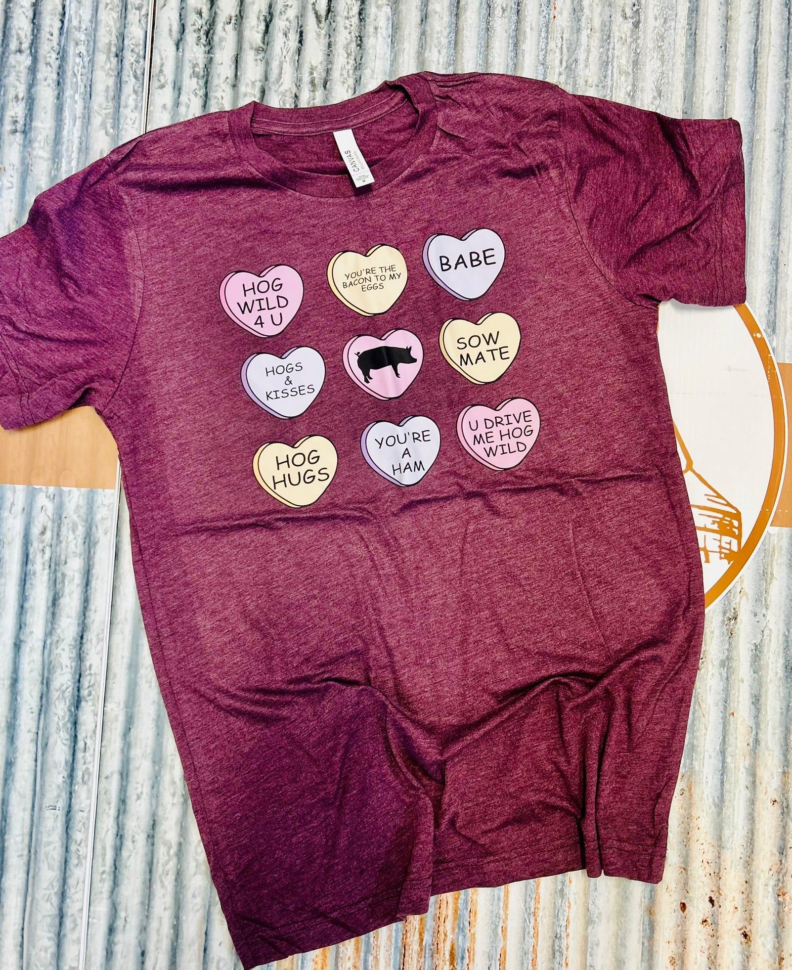 Maroon t-shirt with colorful heart-shaped text design on a textured surface