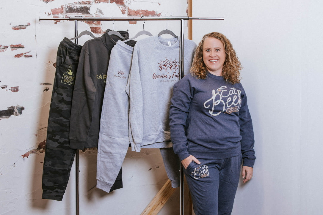 Woman standing next to a rack of sweatshirts with various designs on a white wall.